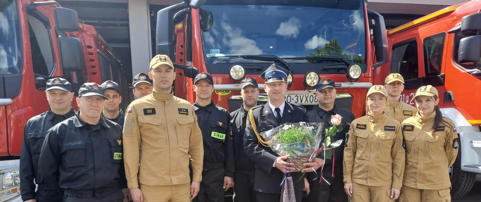Powołanie Komendanta Powiatowego Państwowej Straży Pożarnej w Kościanie. Funkcjonariusze stoją w rzędzie przed strażnicą, za nimi budynek Komendy i samochód strażacki. 