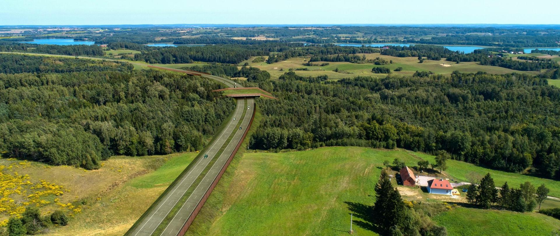 Widoczna droga biegnąca przez zieloną, pagórkowatą okolicę. Droga przecina się z wiaduktem. W tle rozciąga się szeroki widok na lasy, pola oraz jeziora. Po prawej stronie w dolnej części obrazu znajduje się zabudowa wiejska z charakterystycznym czerwonym dachem.