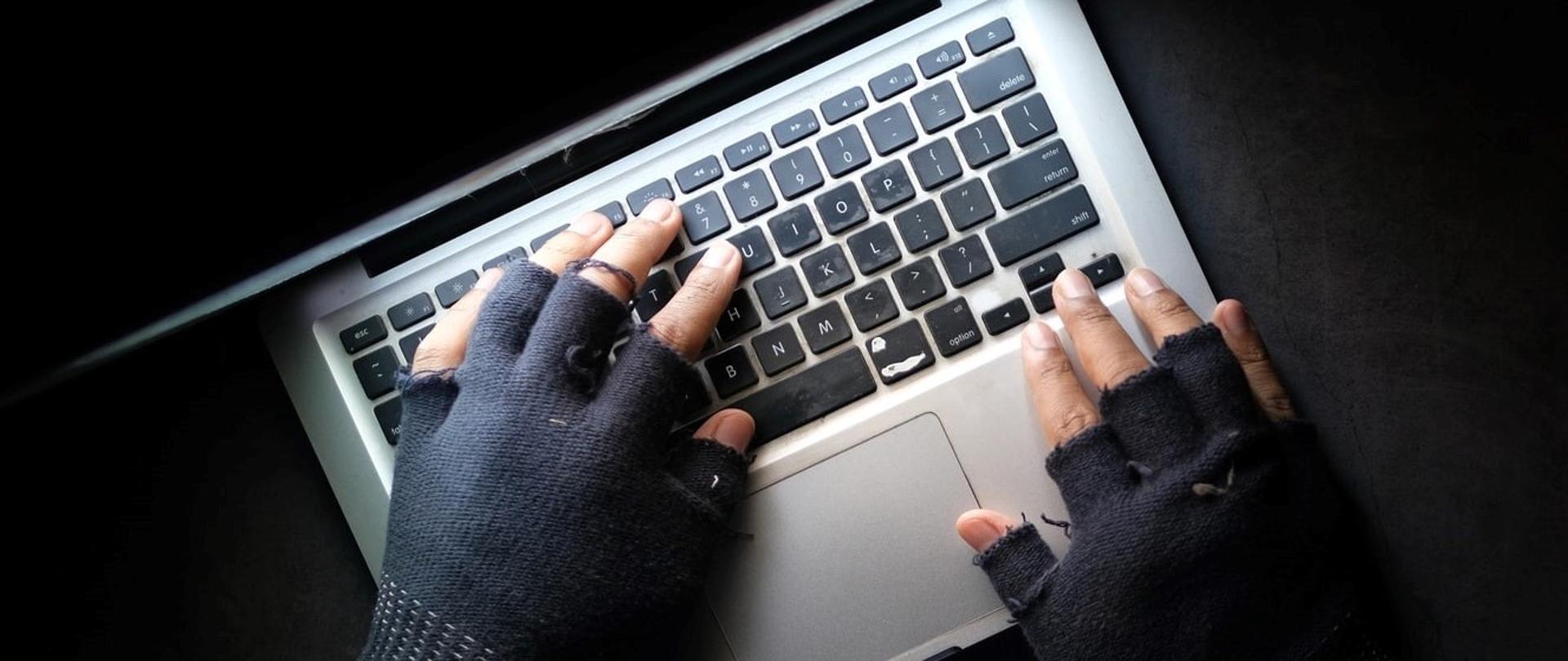 Dłonie w rękawiczkach na klawiaturze laptopa