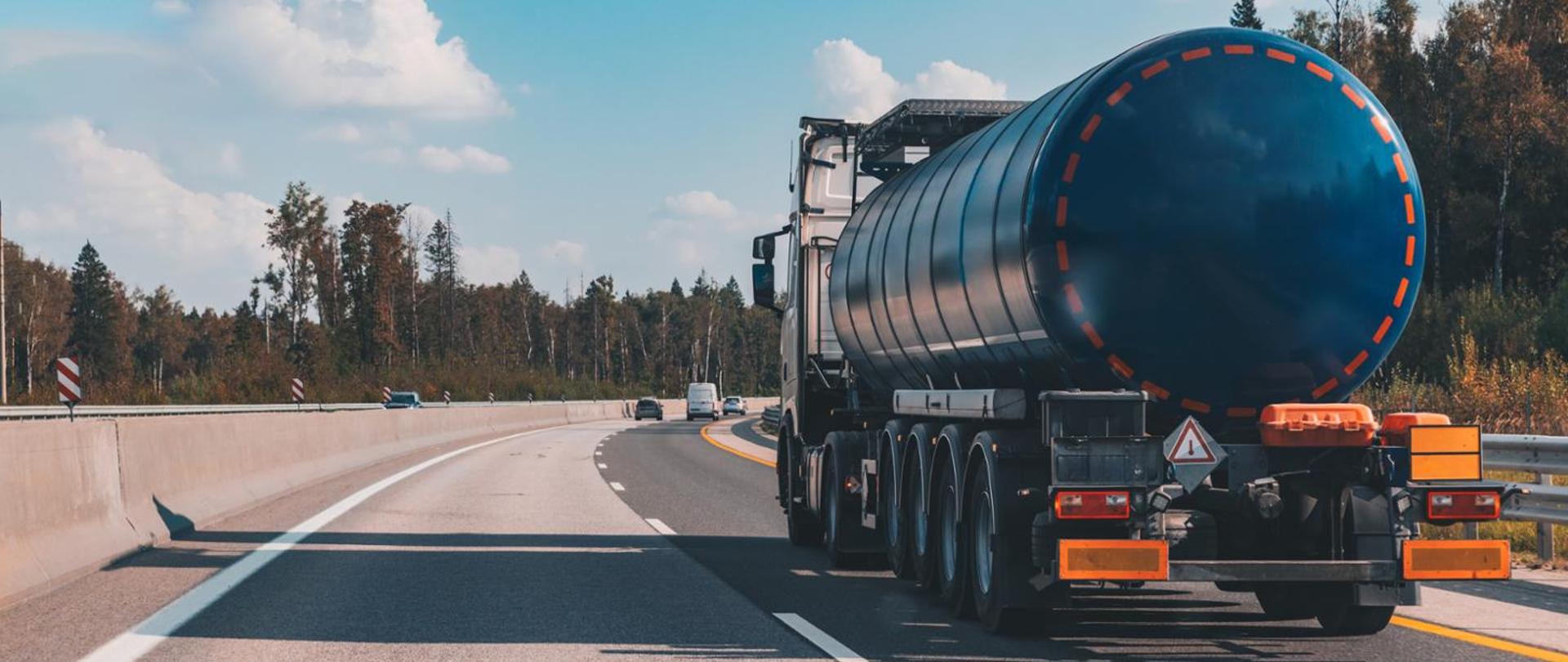 Ciężarówka-cysterna na dwupasmowej drodze szybkiego ruchu, przed nią kilka samochodów, wokół przydrożne drzewa. Fot.: Ministerstwo Infrastruktury.