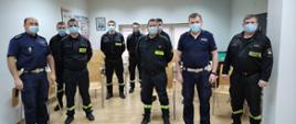 wspólne zdjęcie strażaków i Policjantów. wszyscy stoją, strażacy w umundurowaniu koszarowym. wszyscy mają maseczki ochronne, w zdjęcie w świetlicy KP PSP.