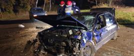 Nocny wypadek na drodze Ponin - Czacz. Na zdjęciu rozbity samochód. W tle strażacy i policjant.
