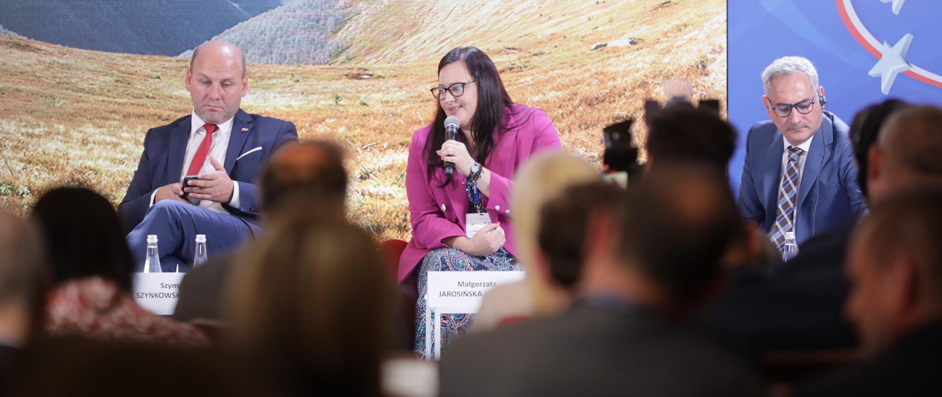 Trzech panelistów siedzi przy niskich stolikach. W środku wiceminister Małgorzata Jarosińska-Jedynak z mikrofonem.