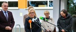 Ministra klimatu i środowiska Paulina Hennig-Kloska podczas konferencji prasowej w Szkole Podstawowej nr 14 w Zielonej Górze. Na zdjęciu ministra stoi przed budynkiem szkoły i mówi do mikrofonów dziennikarzy. Za nią stoi kilka osób.