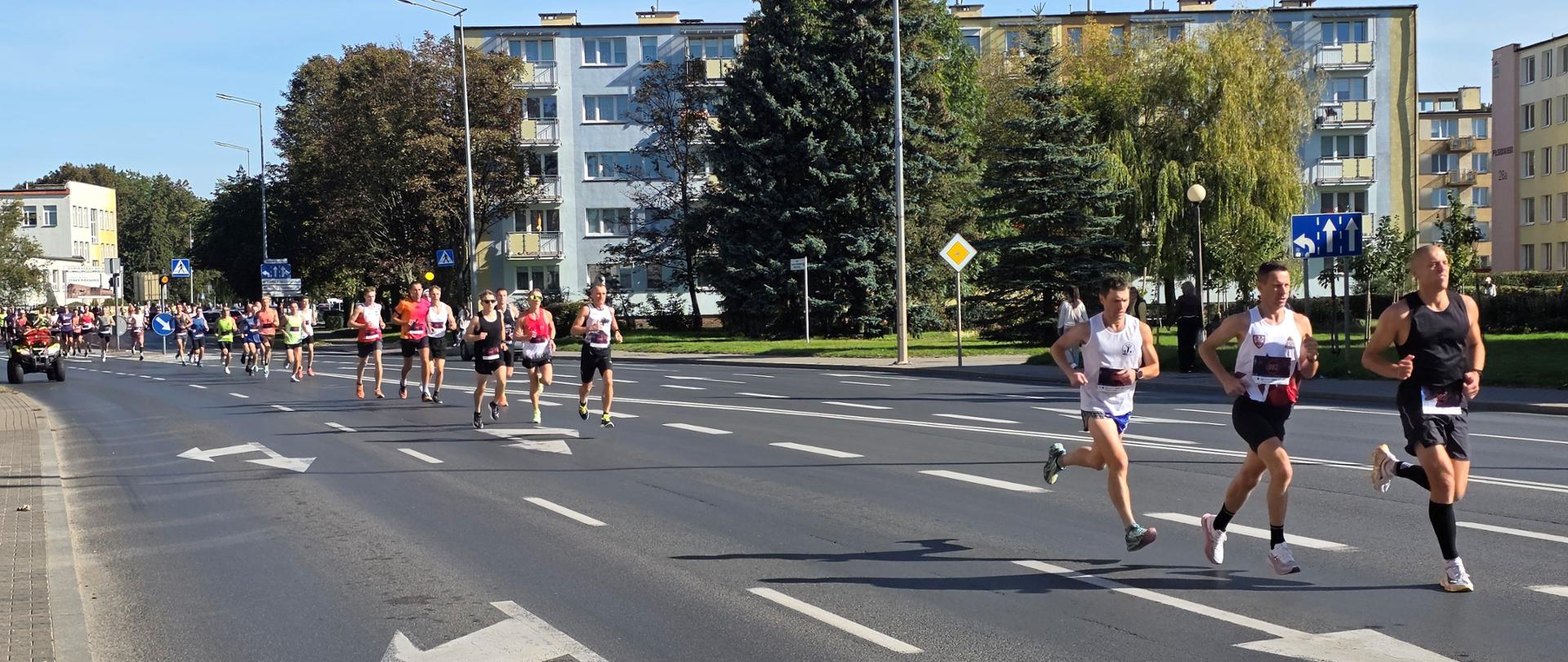 Zawodnicy w kolorowych strojach sportowych biegnący ulicami miasta