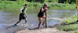 dwoje zawodników wychodzi z rzeki, dziewczyna trzymając się palika do którego przymocowana jest lina asekuracyjna
