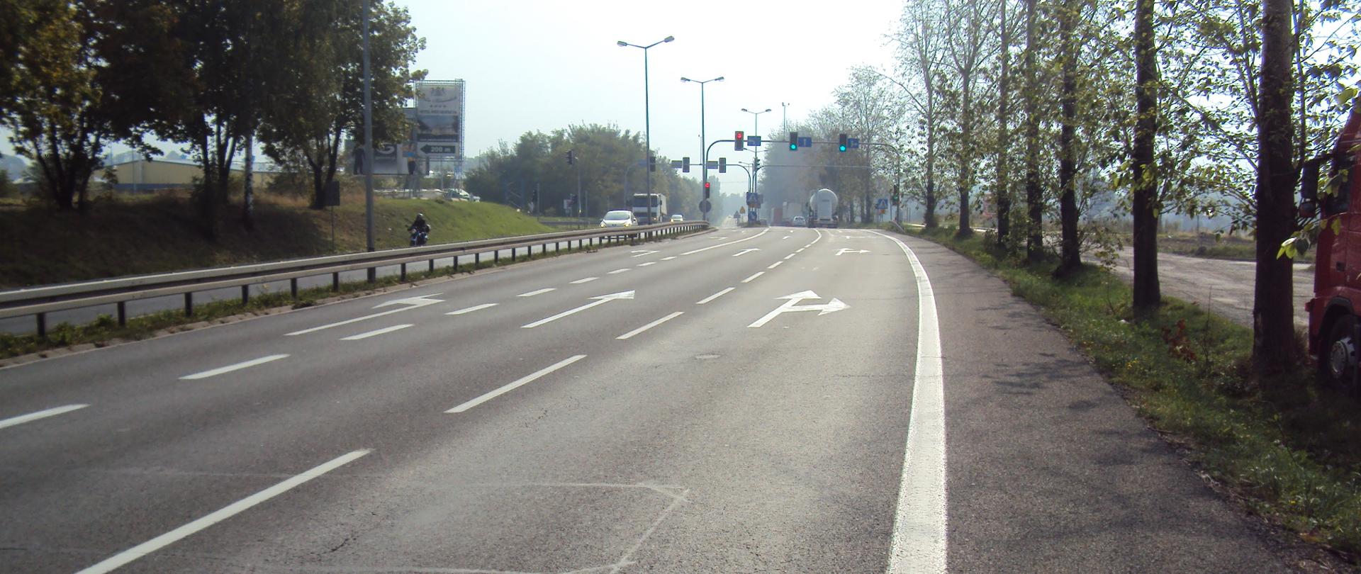skrzyżowanie DK91, zdjęcie przedstawia skrzyżowanie czterowlotowe wyposażone w sygnalizację świetlną na drodze dwujezdniowej a dwóch pasach ruchu w każdym kierunku