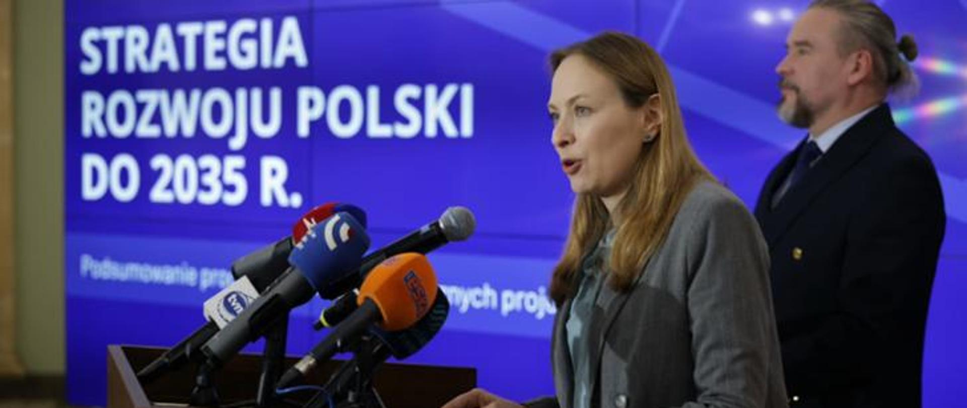 In the photo, Minister Katarzyna Pełczyńska-Nałęcz stands in front of microphones, in the background you can see the Polish and EU flags