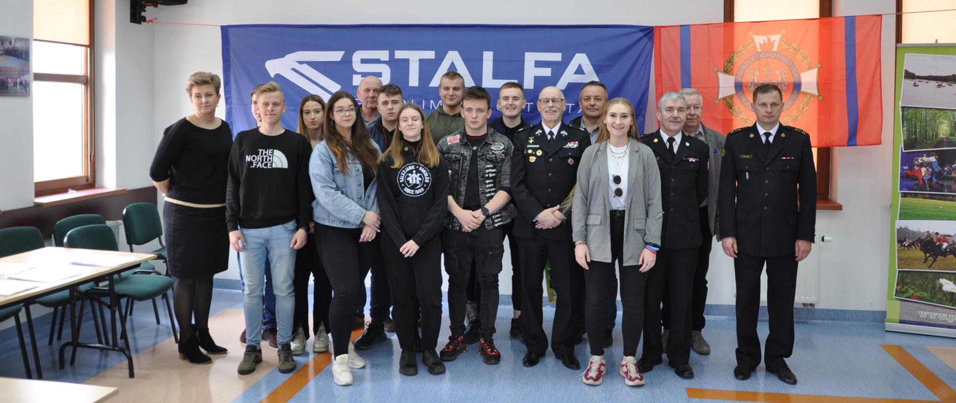 Eliminacje powiatowe Ogólnopolskiego Turnieju Wiedzy Pożarniczej 2022 - uczestnicy turnieju razem z jury stoją w sali w KP PSP