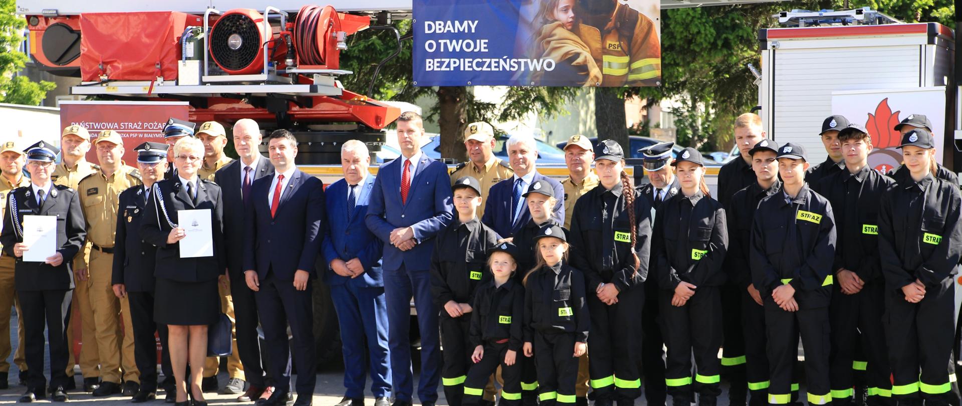 Zdjęcie grupowe uczestników wydarzenia na tle pojazdu pożarniczego. 