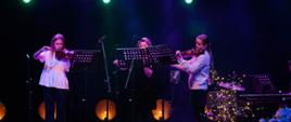 Zdjęcie przedstawia Zespół Skrzypcowy PSM I stopnia w Jarocinie złożony z trzech uczennic klasy skrzypiec występujących na scenie podczas koncertu świątecznego.