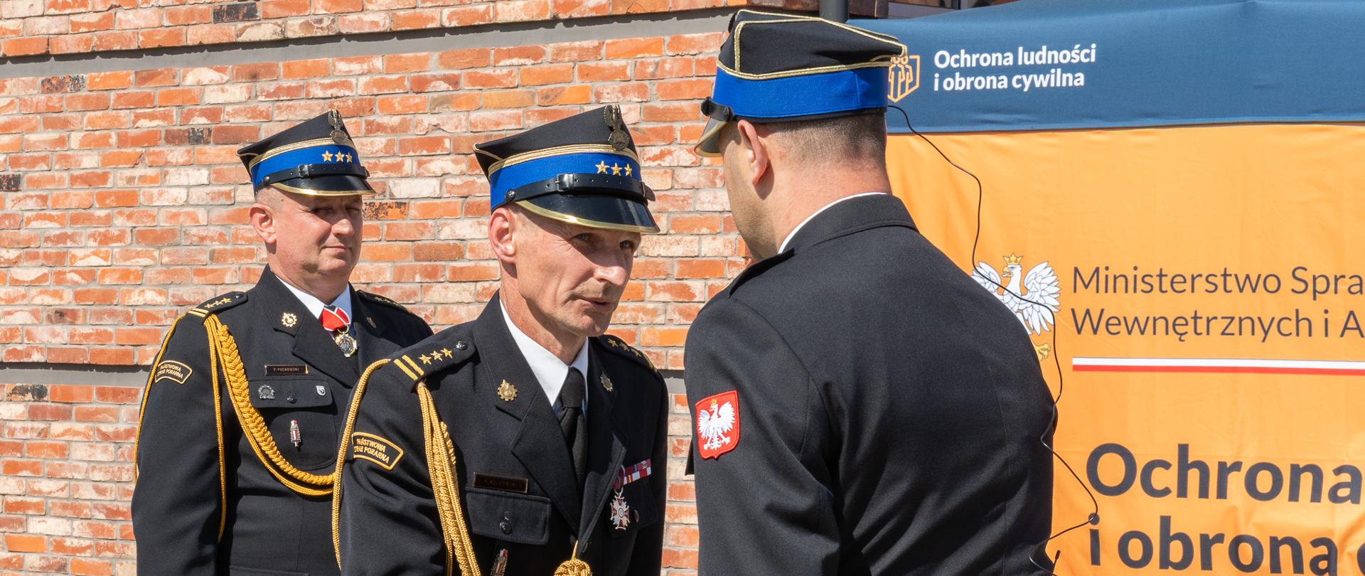 Na zdjęciu dowódca uroczystości młodszy kapitan Krystian Kaczmarek składający meldunek zastępcy Kujawsko Pomorskiego Komendanta Wojewódzkiego starszemu brygadierowi Robertowi Kulasińskiemu. W tle starszy brygadier Paweł Puchowski Komendant Powiatowy Państwowej Straży Pożarnej w Świeciu