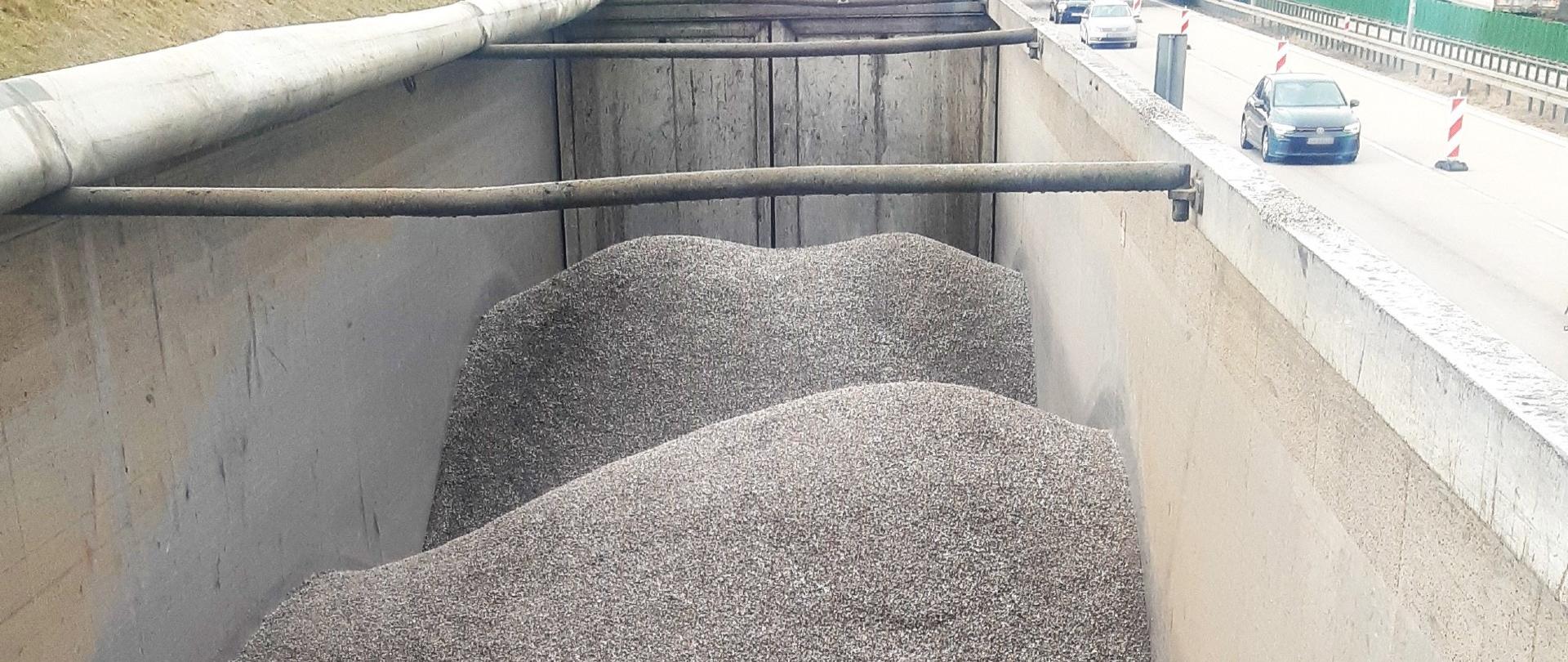 Otwarta naczepa ciężarówki wypełniona dużą ilością drobnego kruszywa.