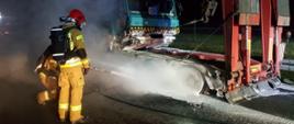 Naczepa samochodowa ze spalonymi oponami obok strażacy gaszą.