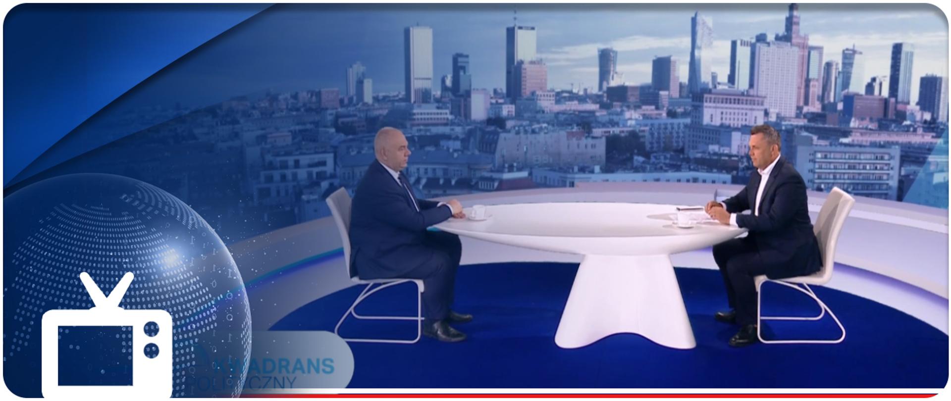 Wicepremier Jacek Sasin i redaktor Jacek Łęski siedzą przy stole w studiu telewizyjnym. W lewym dolnym rogu ikonka telewizora. 
