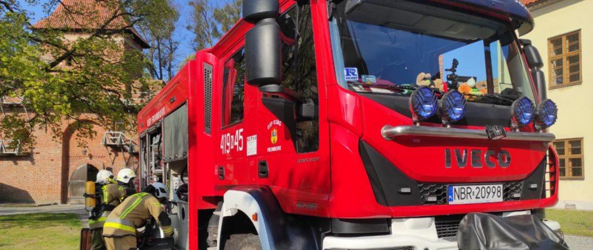 Na zdjęciu duży czerwony samochód z OSP Frombork, z lewej strony strażacy.