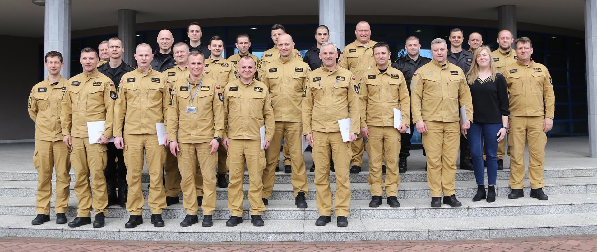 Grupowe zdjęcie uczestników szkolenia (19 funkcjonariuszy PSP) w towarzystwie Zastępcy Komendanta Centralnej Szkoły PSP, kobiety oraz czterech oficerów Centralnej Szkoły PSP