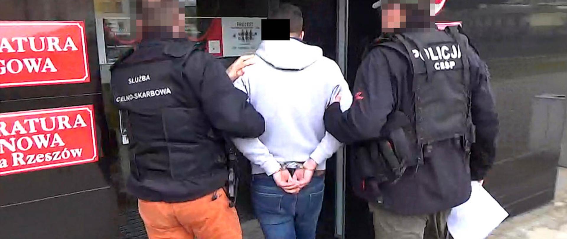 Funkcjonariusze Służby Celno-Skarbowej i CBŚP prowadzą zatrzymanego mężczyznę.