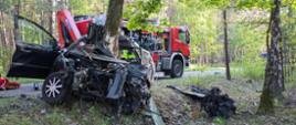 Zniszczony pojazd, w tle samochód straży pożarnej.