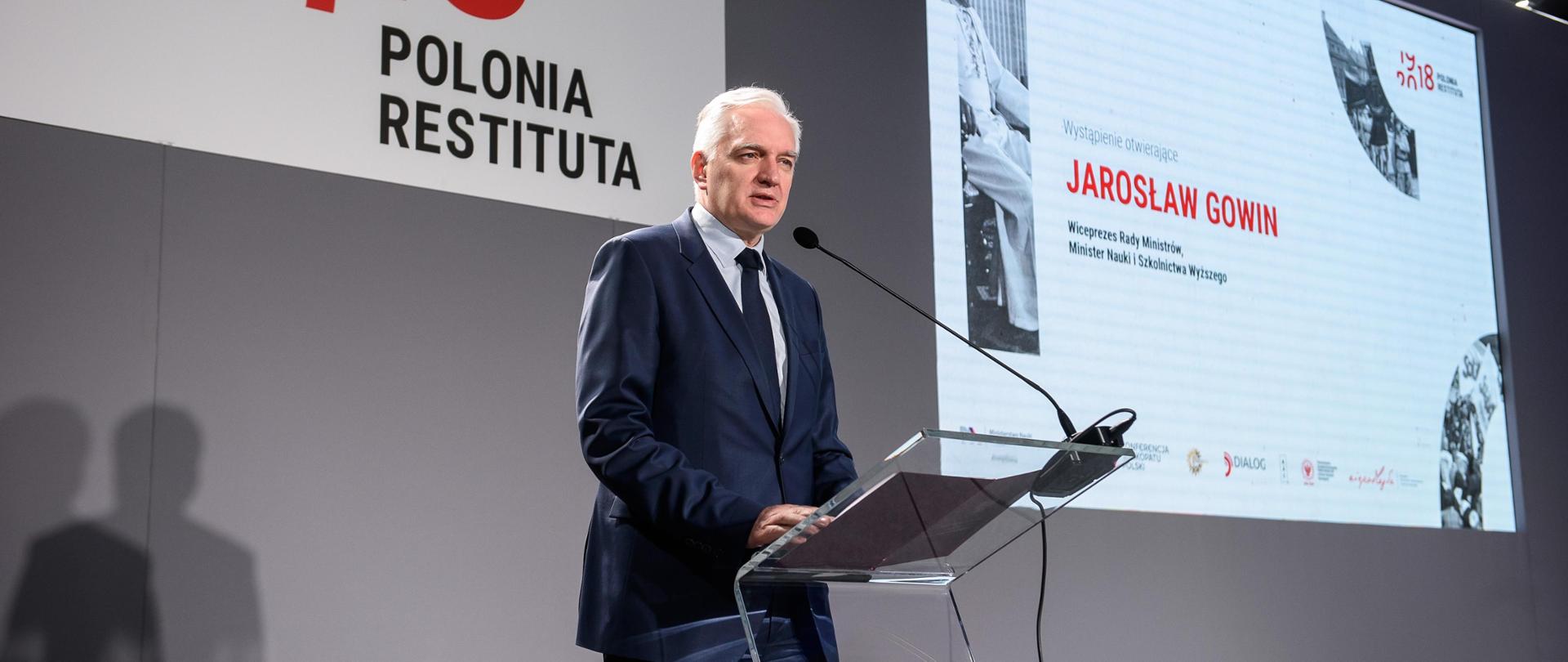 Minister Gowin przemawia do mikrofonu, w tle logo Polonia Restituta - napis i stylizowane daty 1918 - 2018