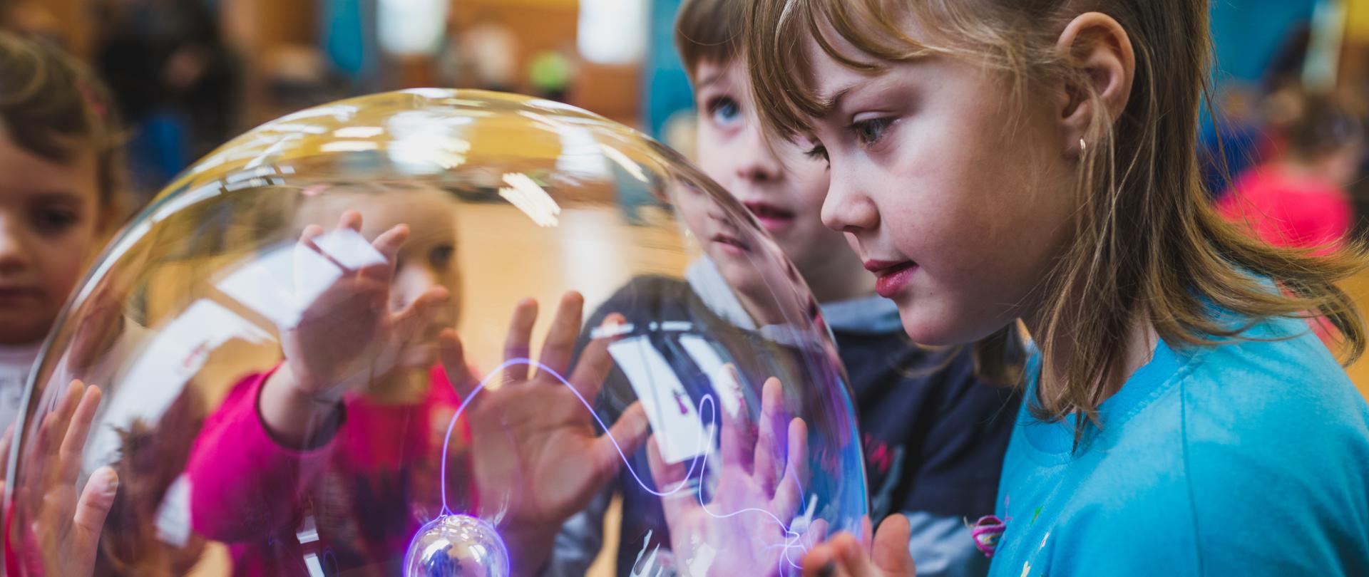 Dziewczynka patrzy na kulę plazmową, w tle inne dzieci