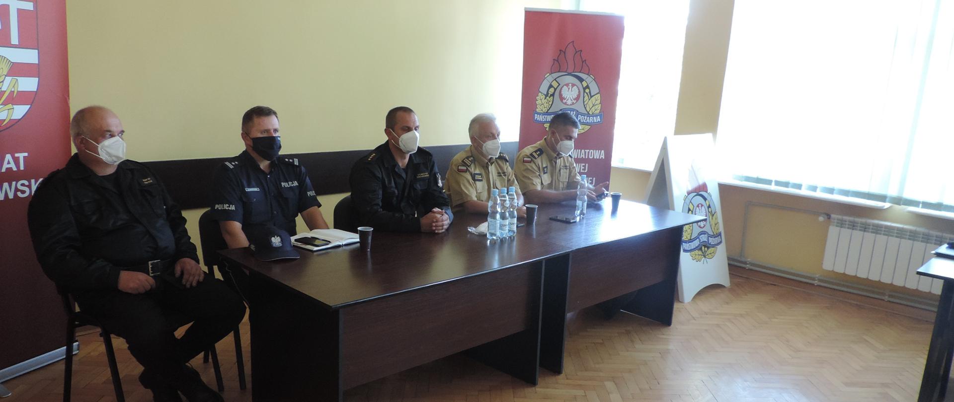 W sali szkoleniowej umundurowani strażacy siedzący przy stole prezydialnym.