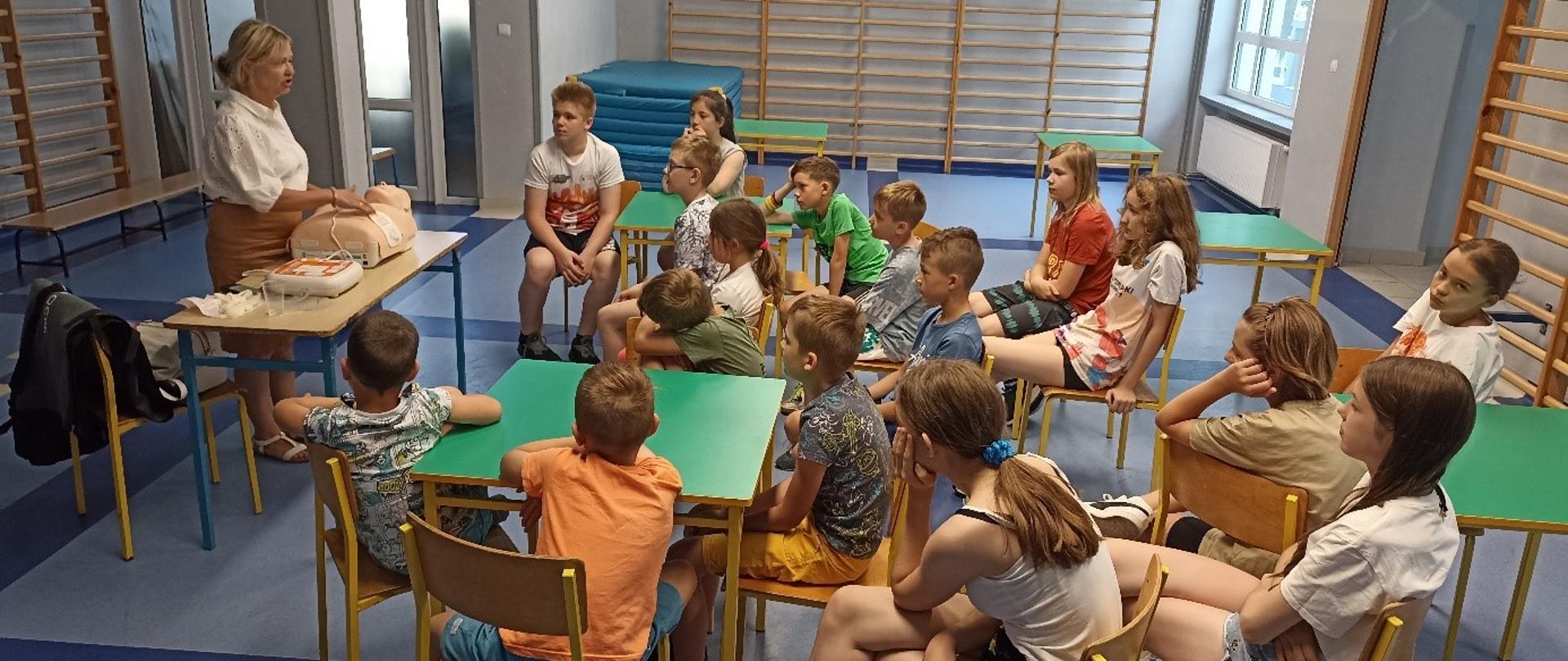 Ruszyła akcja “Bezpieczne Wakacje” - dzieci przy stolikach na sali wykładowej