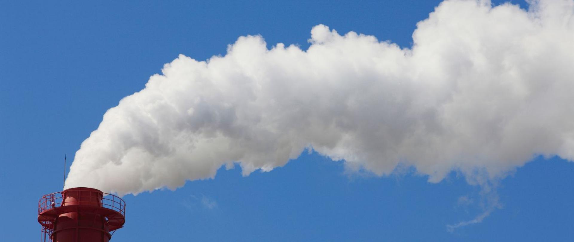 na zdjęciu widnieje komin fabryki, z którego wydobywa się jasny, biały dym.