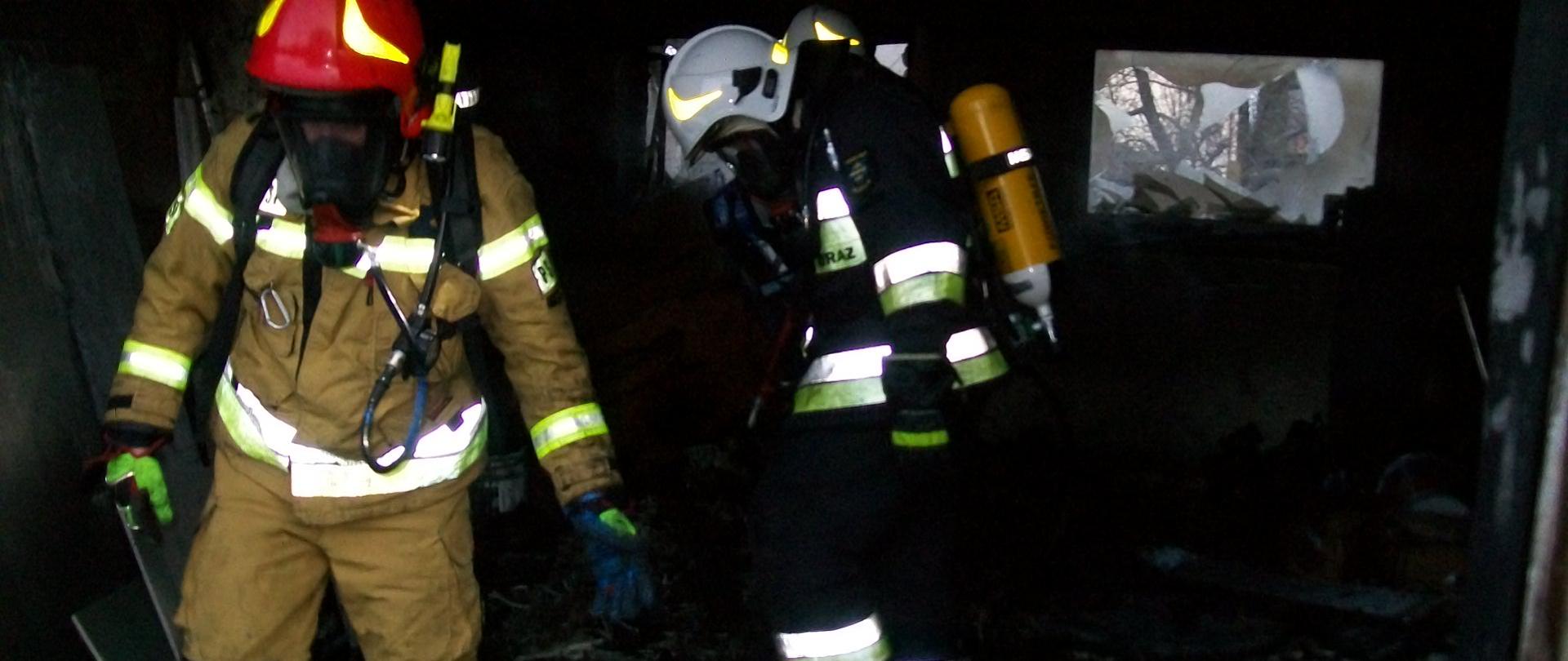 Dwóch strażaków przeszukuje spalone pomieszczenie garażowe