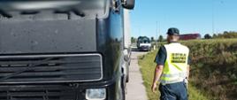 Na pierwszym planie (od lewej): przód i lewy bok kontrolowanego ciągnika siodłowego i naczepy ciężarowej. Obok stoi umundurowany inspektor warmińsko-mazurskiej ITD. W tle: dwa oznakowane furgony ITD stoją w punkcie kontrolnym. Za nimi przejeżdża ciężarówka.