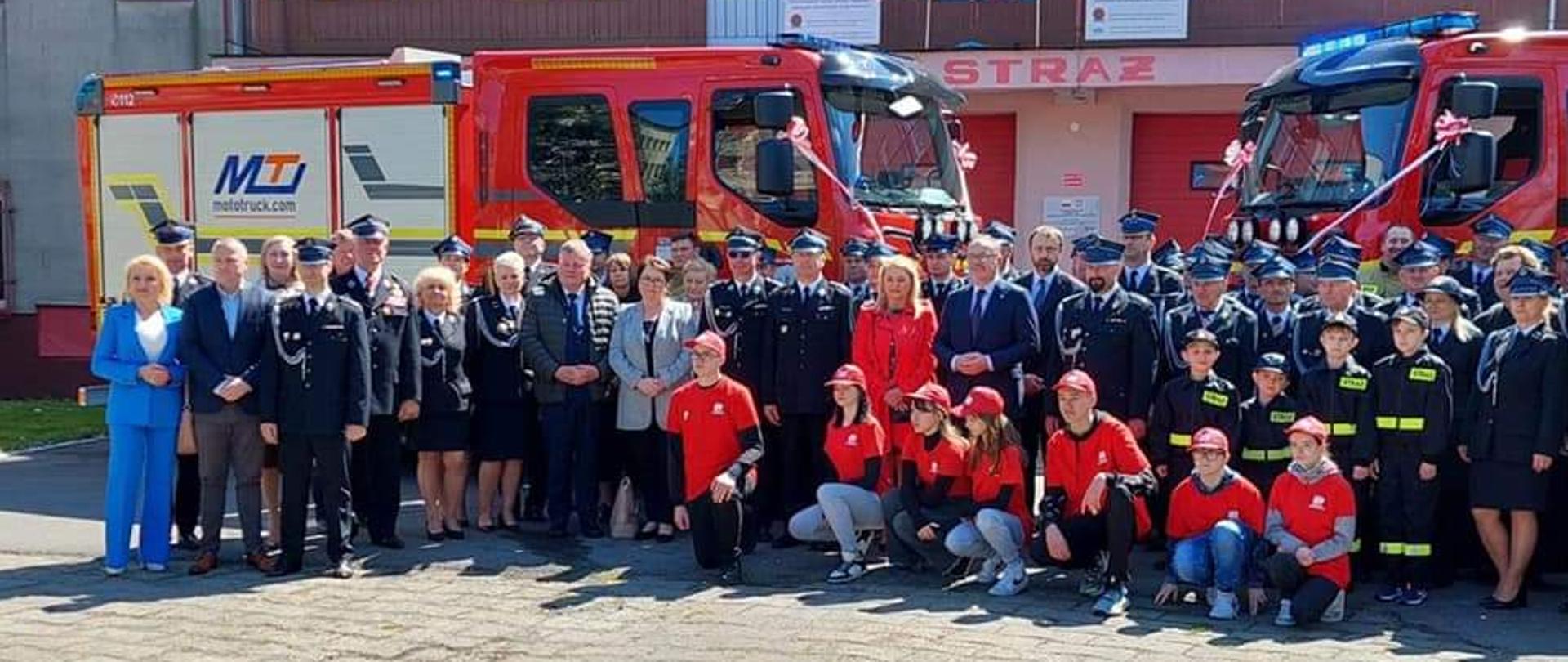 Na zdjęciu przed strażnicą Ochotniczej Straży Pożarnej ustawione dwa świeżo przekazane wizy strażackie. Przed nimi strażacy i goście, którzy brali udział w uroczystym przekazaniu.