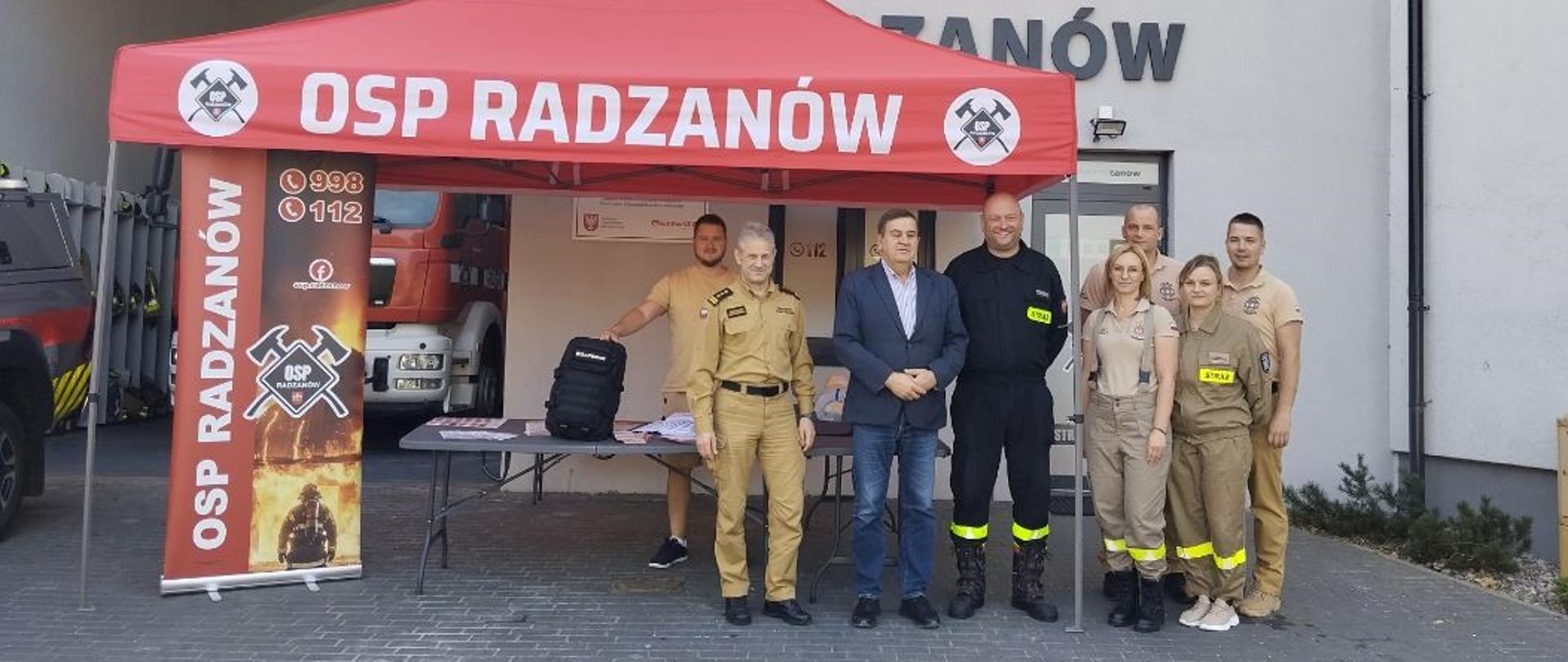 Strażacy OSP Radzanów oraz uczestnicy akcji „Akcja – reakcja!” przed siedzibą jednostki. Podczas wydarzenia mieszkańcy mogli zapoznać się z wyposażeniem strażaków oraz zasadami bezpieczeństwa.