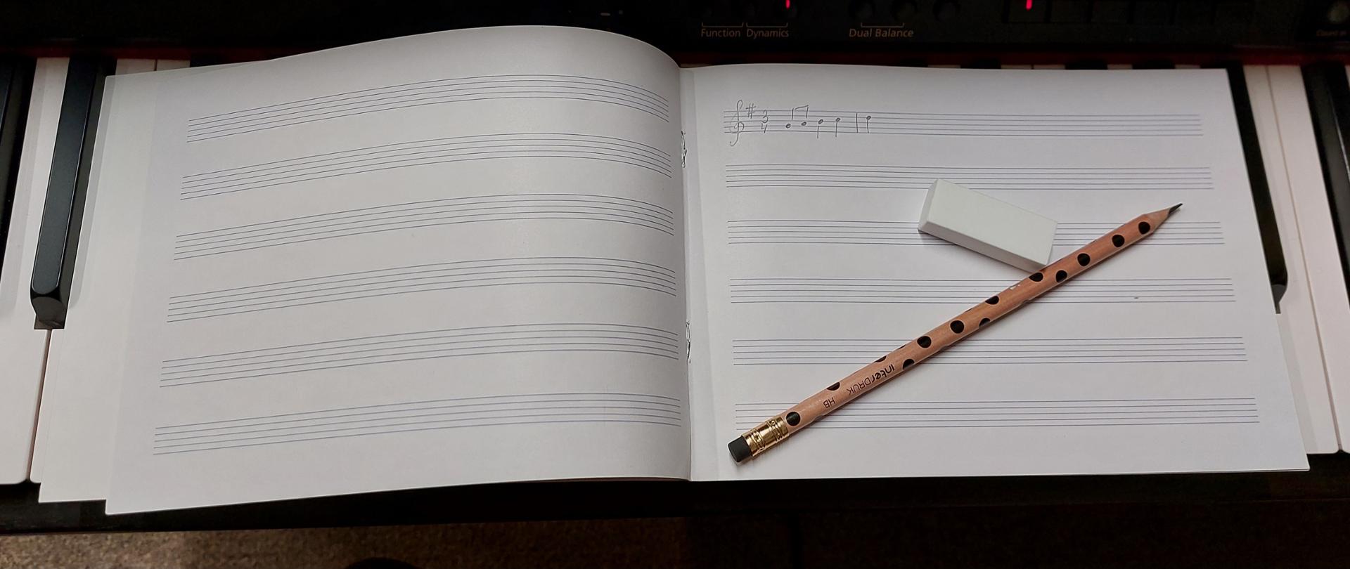 zdjęcie przedstawia klawiaturę fortepianu na której ułożony został zeszyt do nut z ołówkiem i gumką