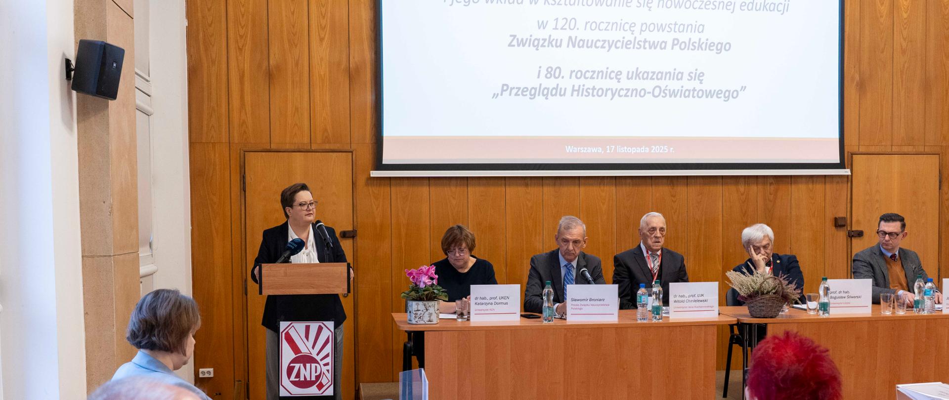 Szerokie ujęcie panelu dyskusyjnego. Katarzyna Lubnauer stoi przy mównicy po lewej stronie, przemawiając. Przy stole panelowym w głębi siedzi pięć osób. Nad nimi wyświetlony jest slajd z tekstem o "120. rocznicy powstania Związku Nauczycielstwa Polskiego" i "80. rocznicy ukazywania się 'Przeglądu Historyczno-Oświatowego'". Na pierwszym planie widoczni są uczestnicy siedzący przy stołach.