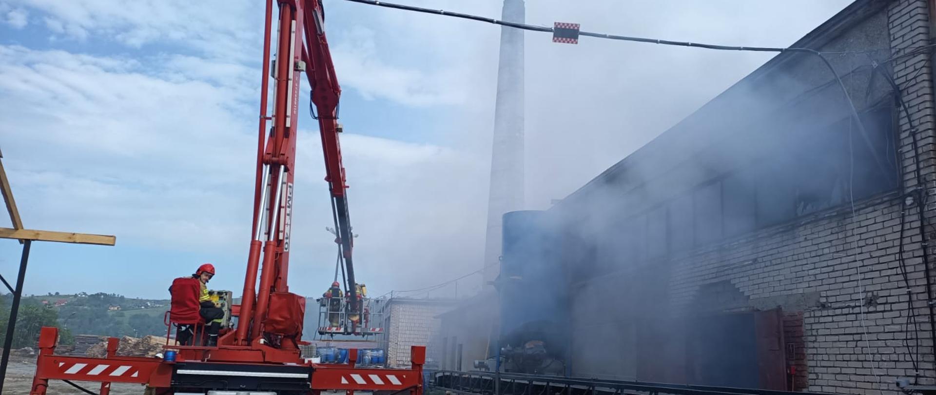 Podnośnik obok budynku z którego wydobywa się dym.
