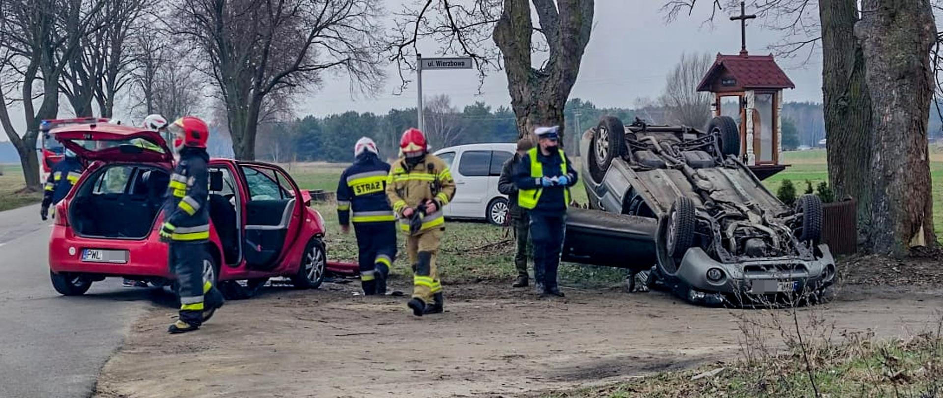 Dwa samochody, jeden na dachu. Obok policjant i strażacy.
