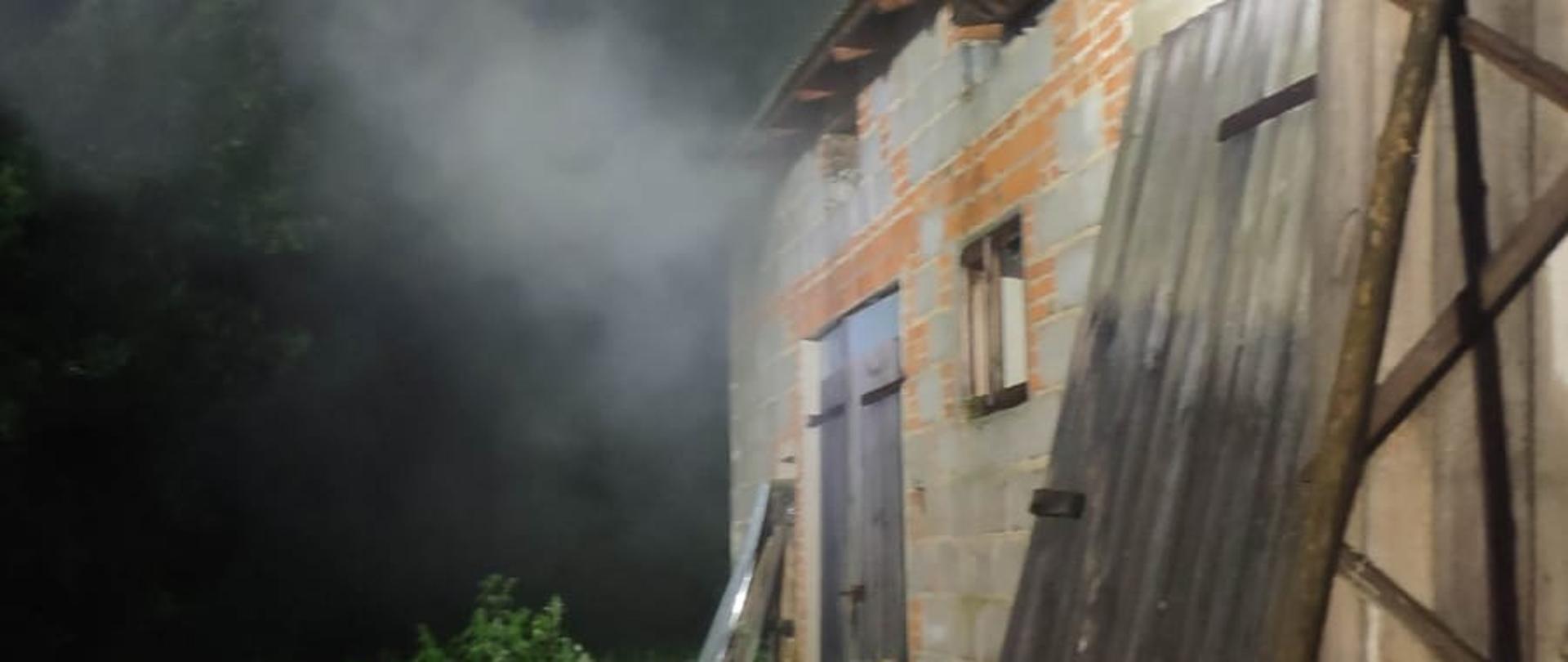 Zdjęcie przedstawia stodołę ceglaną, z której unosi się dym.
