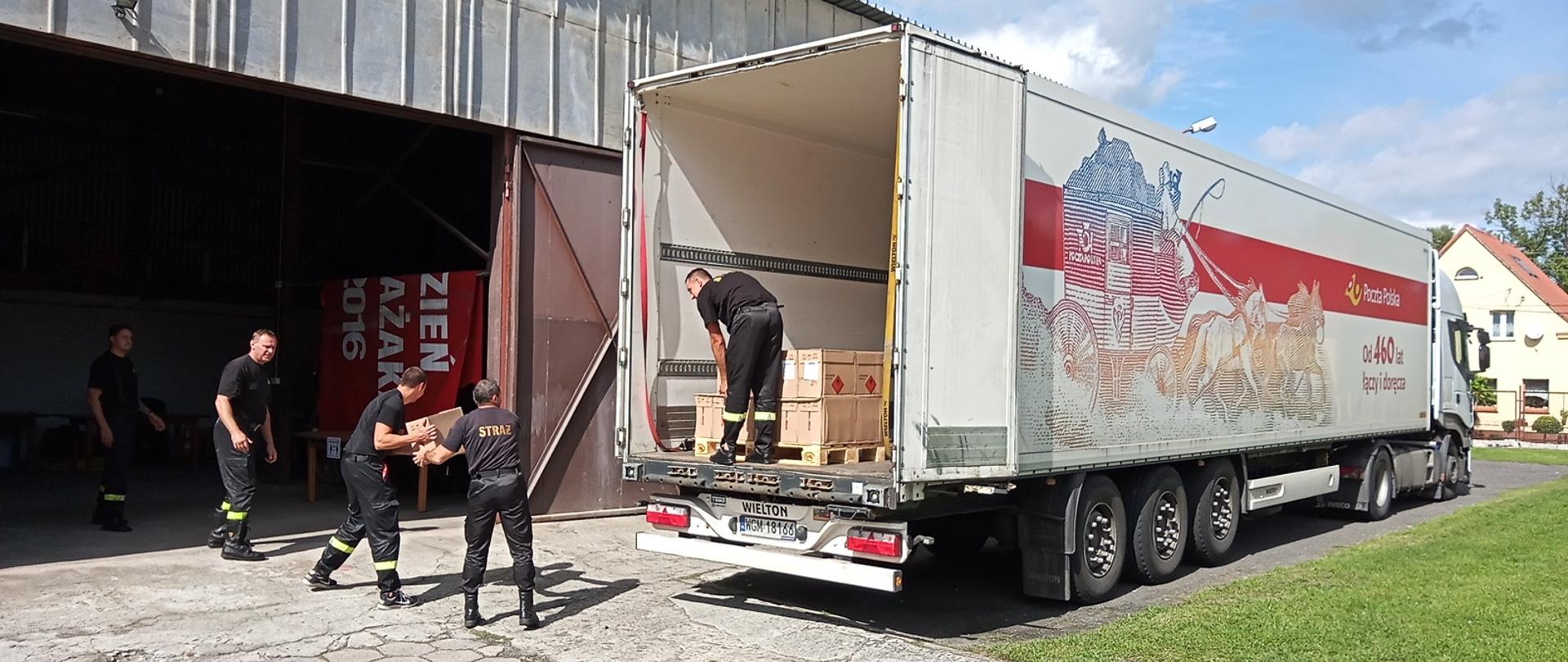 Na zdjęciu widoczni funkcjonariusze przenoszący opakowania z środkami ochrony indywidualnej