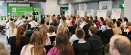Mężczyzna za mównicą na tle zielonych banerów z logo KRUS przemawia do siedzących na krzesłach uczestników wydarzenia.