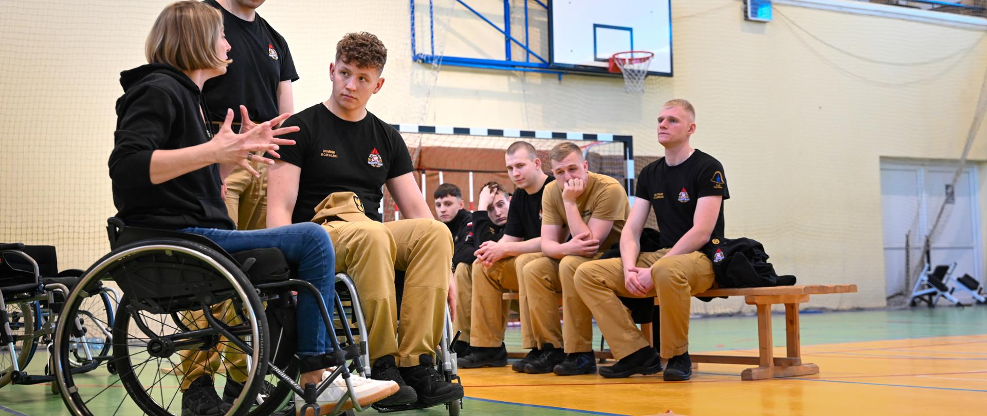 Instruktorka na wózku inwalidzkim omawia zasady bezpiecznej ewakuacji osoby z niepełnosprawnością ruchową podczas zajęć dla kadetów PSP