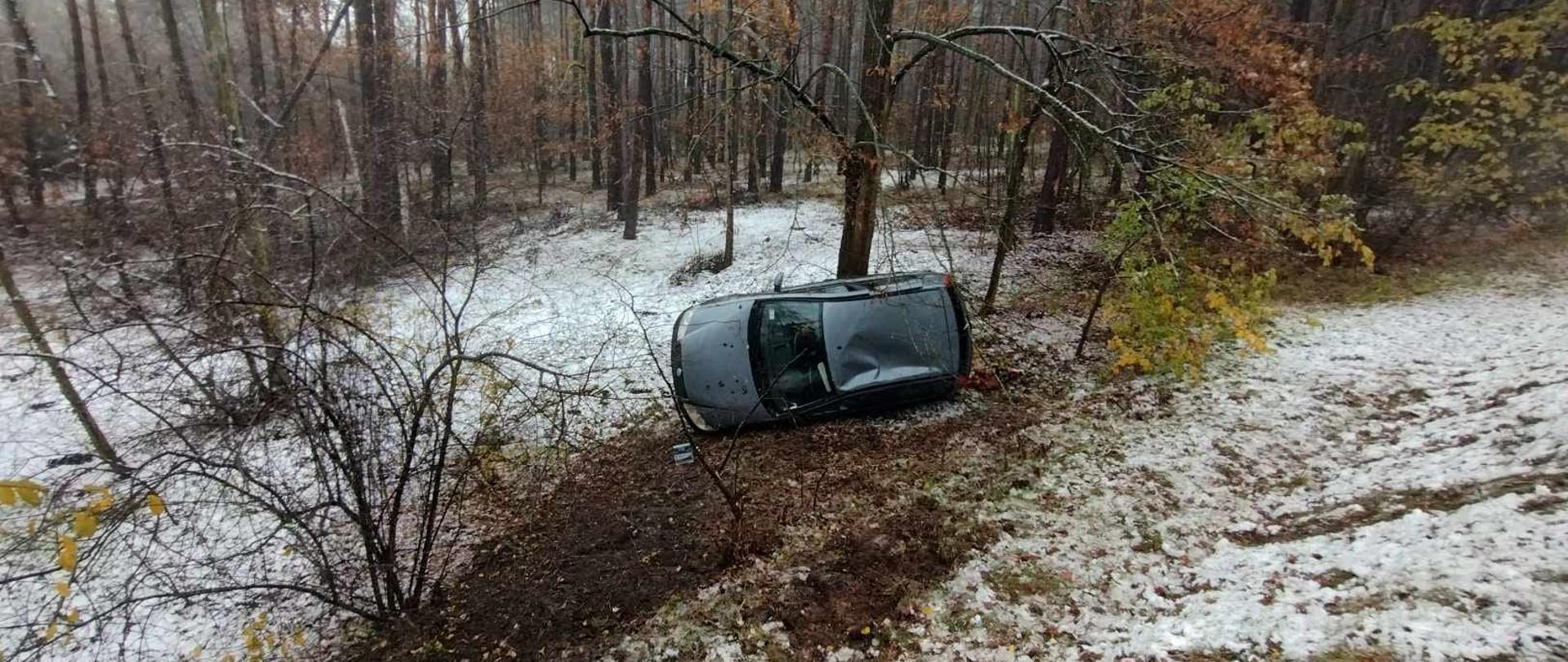 Ciemny samochód na lewym boku przy drzewie, przed nim śnieg