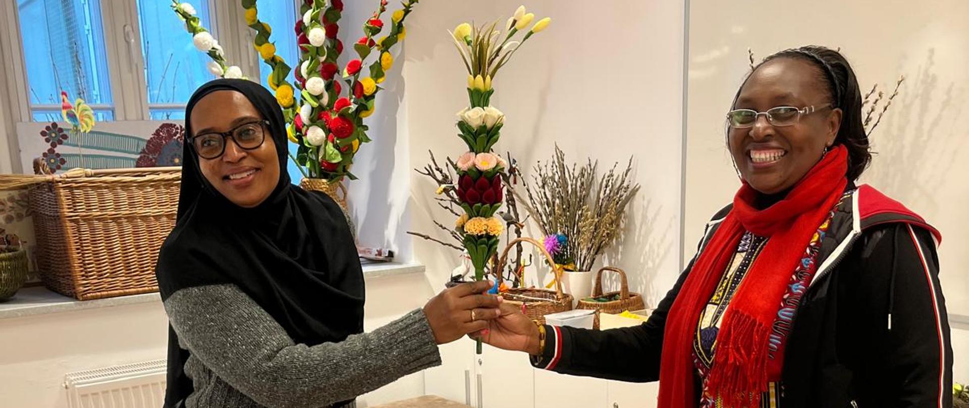 Dwie delegatki z Kenii trzymają w rękach palmę wielkanocną wykonaną z kwiatów w pomieszczeniu Centrum Folkloru Polskiego Karolin.