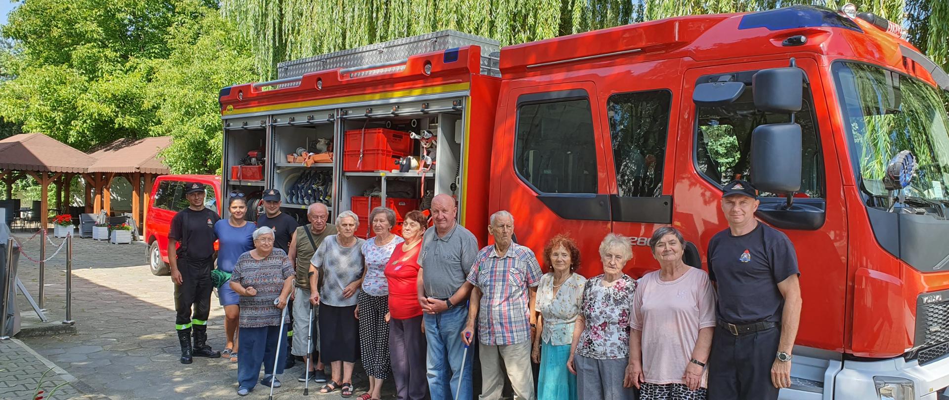 Zdjęcie grupowe strażaków i seniorów, wykonane na tle samochodu pożarniczego