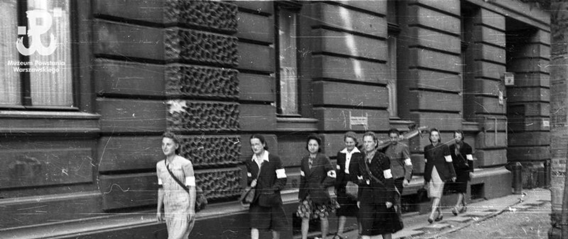 Fotografia z Powstania Warszawskiego. Śródmieście Północne. Grupa sanitariuszek z kompanii "Koszta" przechodząca obok domu przy Moniuszki 9; od lewej: Gabriela Karska "Joasia" , dr Zofia Lejmbach "Róża" , Danuta Laskowska "Dorota", (NN) "Małgorzata", Halina Wojtczuk "Halszka" , Wanda Regenciak "Alicja" , dr Danuta Staszewska "Marta" , z boku idzie Melania Wolska "Ewa Samarytanka"