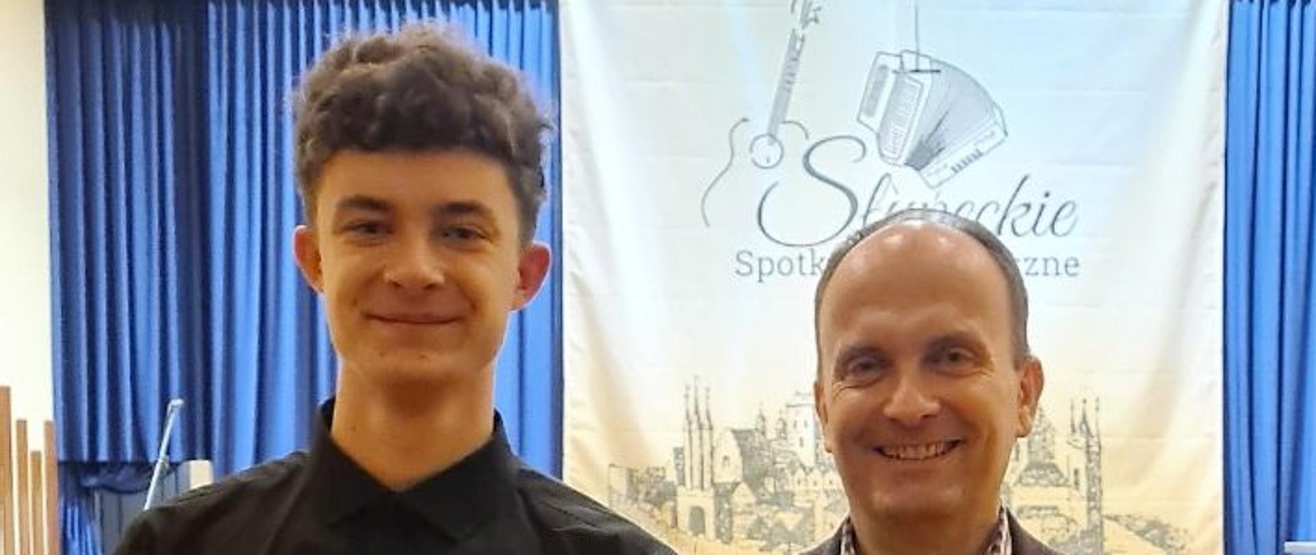 Zdjęcie przedstawia uczestnika konkursu z nauczycielem na tle sceny w PSM w Słupcy.