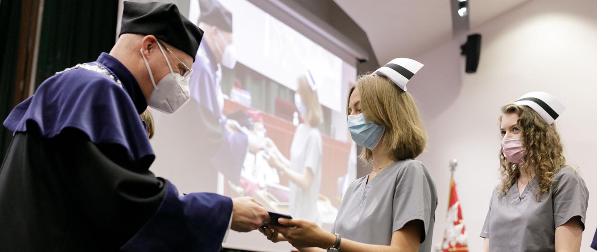 Naz zdjęciu widoczny jest mężczyzna, ubrany w togę oraz dwie kobiety.