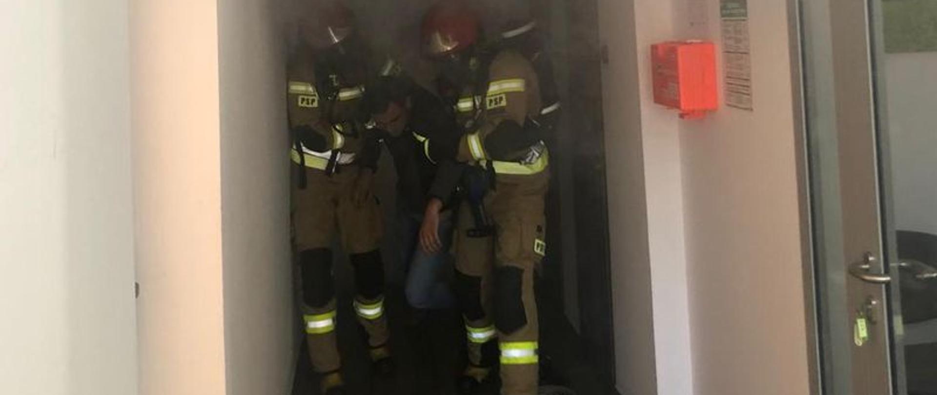 Strażacy wyposażeni w sprzęt ochrony dróg oddechowych w zadymieniu odnajdują osobę poszkodowaną