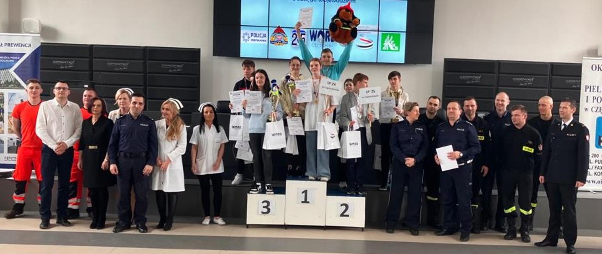 Zdjęcie grupowe uczestników konkursu na podium obok podium komisja i zaproszeni goście.