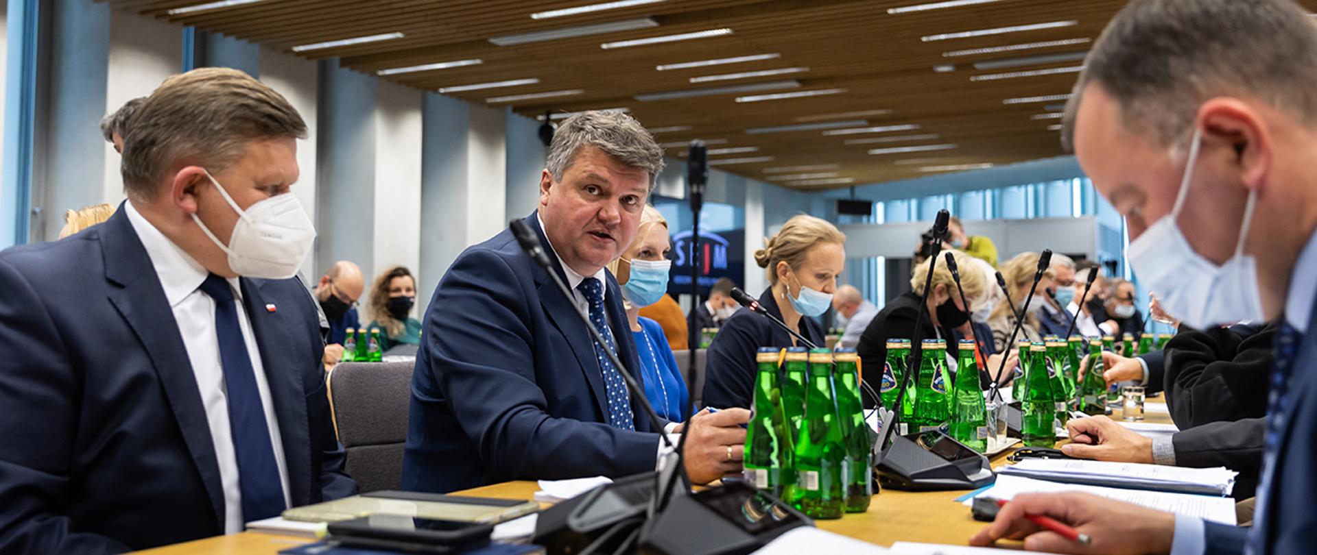 Na zdjęciu widać wiceministra Macieja Wąsika w trakcie wystąpienia na wspólnym posiedzeniu Komisji Obrony Narodowej i Komisji Administracji i Spraw Wewnętrznych siedzącego na sali wśród innych uczestników posiedzenia.