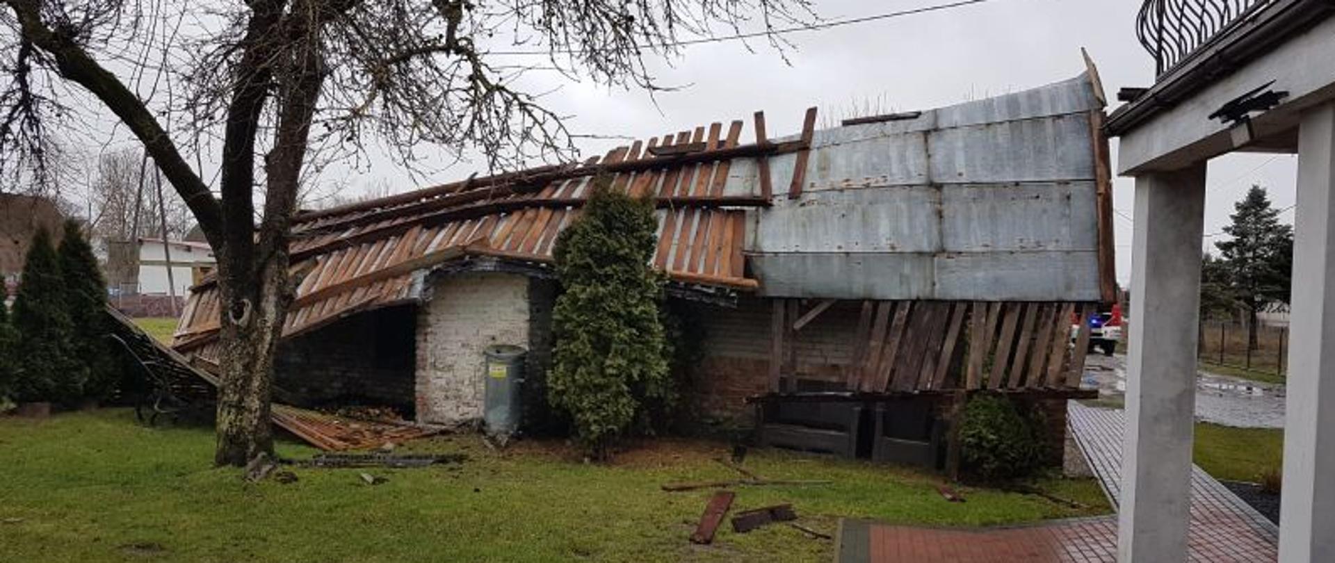 Zdjęcie wykonane w dzień. Przedstawia zerwany dach. Dach jest wykonany z blachy. Jest uszkodzony i wygląda tak jak by zerwał się w całości.